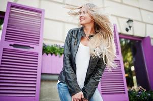 mulher loira elegante usa jeans e jaqueta posou na rua contra a janela roxa. retrato de modelo urbano de moda. foto