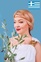 Mulher alegre loira grega em um vestido nacional com um ramo de oliveira falso nas mãos foto
