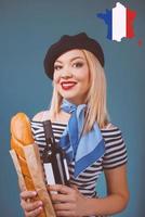 retrato de uma linda mulher loira francesa com boina, lenço, costas e camisa branca, com garrafa de vinho e pão baguete nos braços com a bandeira da França no fundo foto