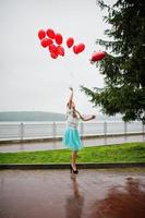 retrato de uma linda linda dama de honra em um lindo vestido segurando balões vermelhos em forma de coração no parque na festa de despedida de solteira. foto