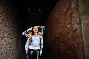 olhar de mulher elegante com paletó listrado preto e branco, calça de couro, posando no velho túnel de tijolo vermelho de rua. conceito de menina da moda. foto