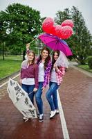 grupo de três meninas se divertindo na festa de galinha, com guarda-chuva sob chuva e balões. foto