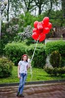 retrato de uma linda dama de honra linda em roupas casuais, segurando balões vermelhos em forma de coração no parque na despedida de solteira. foto