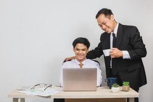 amigável chefe asiático segurando uma xícara e seus funcionários no ombro que trabalham na mesa do escritório foto