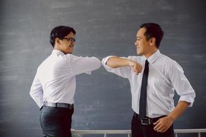 dois empresários asiáticos em camisas brancas fazendo cotoveladas para evitar o vírus corona foto
