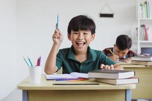 menino de escola primária asiático inteligente e feliz estudando na classe foto