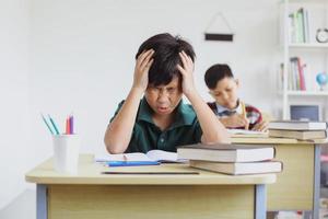 menino do ensino fundamental cansado e estressado fazendo exames em sala de aula foto