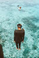 um homem de roupa de mergulho pulando com estilo de pé no mar transparente com muitos peixes do mar foto