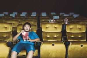 menino asiático sozinho vai ao cinema.