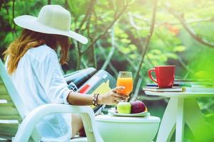 mulher asiática sentada relaxe. ler revistas e beber suco. no Jardim foto