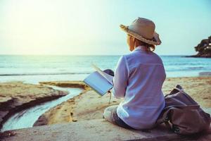 mulher asiática viaja natureza. viajar relaxar estudar ler um livro e escrever uma nota na praia. no verão. tailândia foto