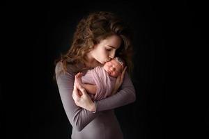 mãe está segurando sua filha recém-nascida. foto tirada em um fundo escuro.
