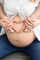 futuro pai mostra coração de dedos na barriga de sua esposa grávida foto