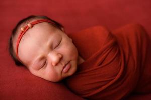 menina recém-nascida dormindo em um pano vermelho em um invólucro vermelho foto
