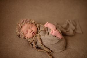 uma menina recém-nascida dorme em um embrulho marrom sobre um fundo de tecido marrom.