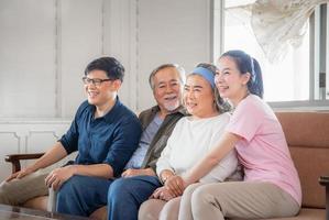 família asiática sentada no sofá e assistindo televisão na sala de estar, pai sênior mãe e filho e filha de meia idade, conceitos de família de felicidade foto