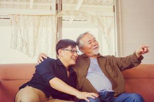 pai asiático sênior e filho de meia idade sentado relaxando e assistindo televisão na sala de estar, conceitos de família asiática de felicidade foto