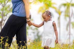 mãe afro-americana segurando a mão de sua filha andando no parque foto