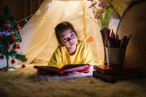 menina lendo um livro na barraca, criança feliz brincando em casa, criança adorável engraçada se divertindo no quarto das crianças. foto