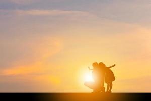 silhuetas de feliz pai e filha brincando no fundo do céu à noite por do sol. foto
