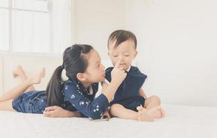 irmã e irmãozinho brincando na cama, família feliz e crianças brincam conceito foto