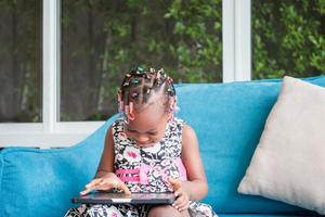 alegre garota afro-americana jogando no tablet na sala de estar foto