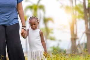 mãe afro-americana segurando a mão de sua filha andando no parque foto