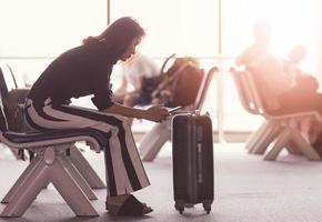 mulher sentada no saguão do aeroporto usando smartphone e olhando para a tela enquanto aguarda o trânsito. luz do sol brilhando de fora foto