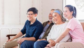 alegre família asiática assistindo televisão na sala de estar, pai sênior mãe e filho de meia idade e filha sentada no sofá, conceitos de família de felicidade foto