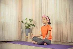 menina bonitinha feliz praticando ioga em casa, conceito de esporte infantil foto