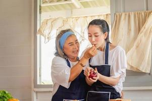 mãe asiática sênior e filha de meia idade cozinhando juntos na cozinha foto