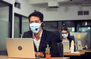 jovem operador de telefone com máscara facial de proteção de fone de ouvido contra coronavírus, equipe executiva de atendimento ao cliente trabalhando no escritório foto