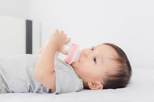 close-up de adorável menino bebendo leite de uma garrafa na cama foto