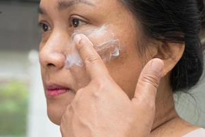 mulher asiática aplicando tratamento de creme para a pele para resolver manchas ou melasma e manchas escuras no rosto. foto