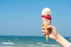 mão segurando casquinha de sorvete com fundo de céu azul foto