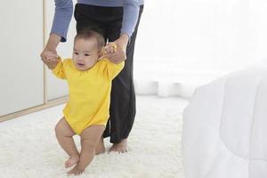 uma mãe asiática está ajudando seu bebê a aprender a andar com alegria. foto