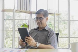 um homem de meia idade asiático usando um ipad na mão. foto
