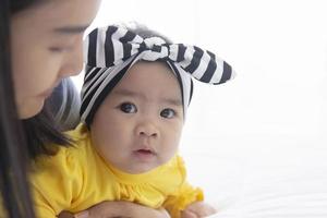 uma mãe asiática brinca com seu bebê na cama com amor e carinho. foto