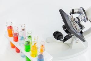 tubos de ensaio em um suporte e um microscópio em uma mesa branca foto
