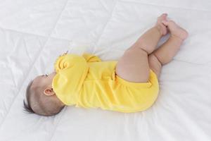 um bebê asiático está dormindo na cama e chupando o leite engarrafado. foto