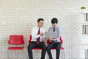 dois homens asiáticos sentam-se em cadeiras de plástico vermelhas à espera de uma entrevista de emprego. foto