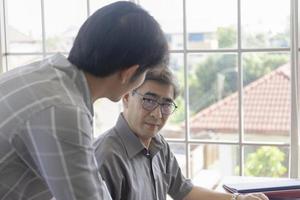 um homem asiático de meia-idade ensinando seu filho a trabalhar ao lado de uma mesa em um escritório. foto