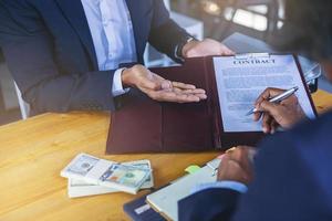 empresário coloca assinatura no contrato na reunião de negócios e passa dinheiro após negociações com parceiros de negócios. foco selecionado foto