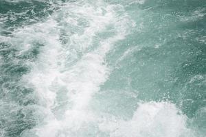 feche a cor turquesa da onda da bolha do fundo do navio remando no oceano para segundo plano. foto