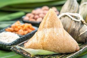 close-up, copie o espaço, famosa comida chinesa no festival do barco dragão duan wu, bolinhos de arroz cozido no vapor em forma piramidal envoltos por folhas de bambu feitas por ingredientes crus de arroz pegajoso foto