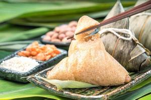 close-up, copie o espaço, famosa comida saborosa chinesa no festival do barco dragão duan wu, bolinhos de arroz cozido no vapor em forma piramidal envoltos por folhas de bambu feitas por ingredientes crus de arroz pegajoso foto