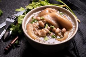 vista superior, close-up, copie o espaço, comida de rua distintiva asiática de taiwan, sopa de joelho de porco de amendoim em uma tigela de cor creme-branca bege marfim isolada na mesa de ardósia de xisto escuro foto