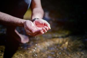 mãos e água fluindo de cachoeiras naturais conceito de água de cachoeira natural foto