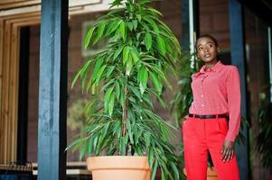 bonito tranças negócio afro-americano senhora brilhante mandão pessoa amigável desgaste escritório vermelho camisa e calças. foto