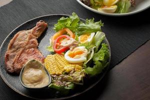 prato de delicioso bife de pernas de frango grelhado com salada de legumes na mesa de madeira foto